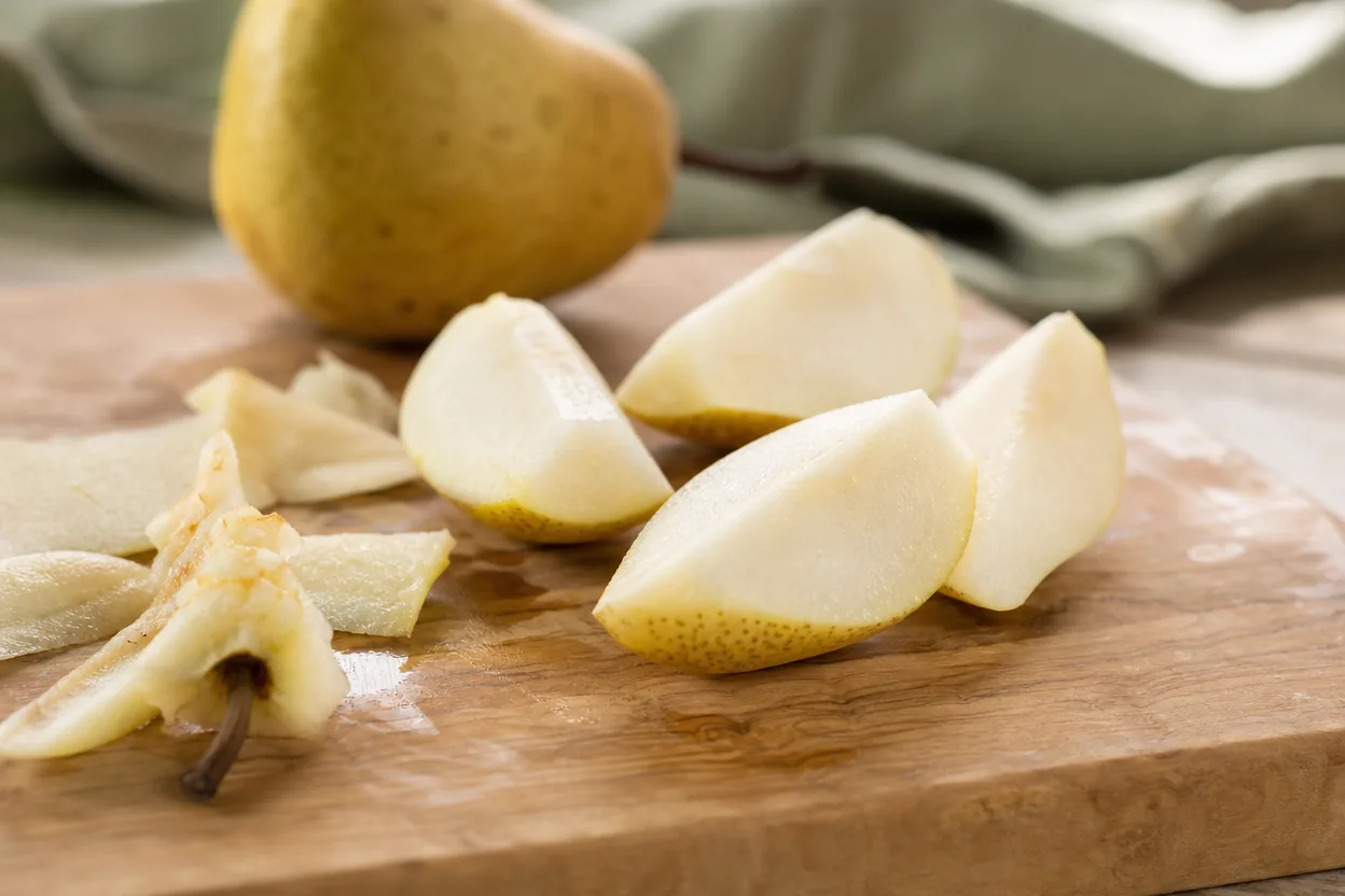 Gros plan d'une poire coupée en morceaux, trognon et pépins retirés, sur une planche en bois